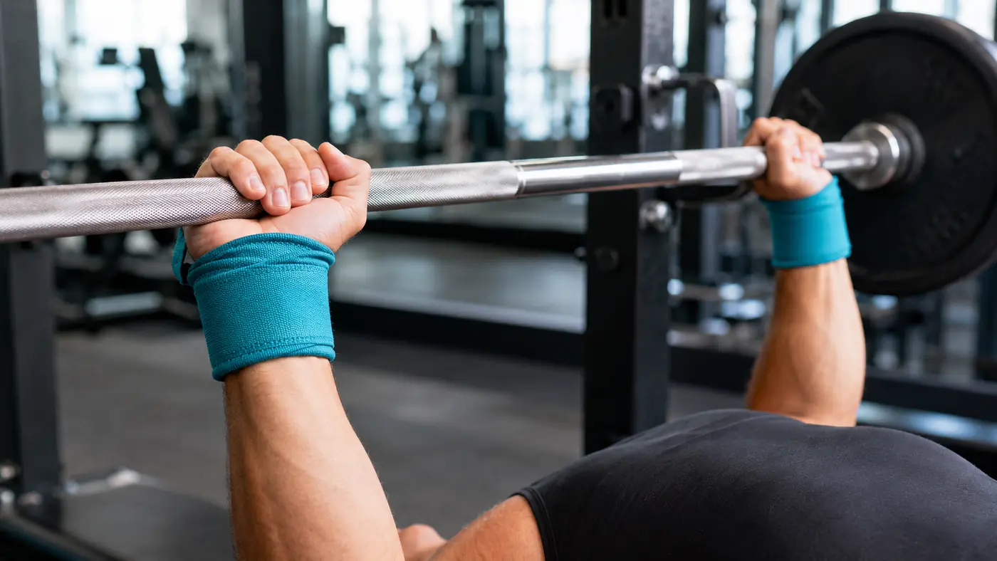 Poignets équipés de bandes de musculation pendant une prise de barre au développé couché en salle de sport.