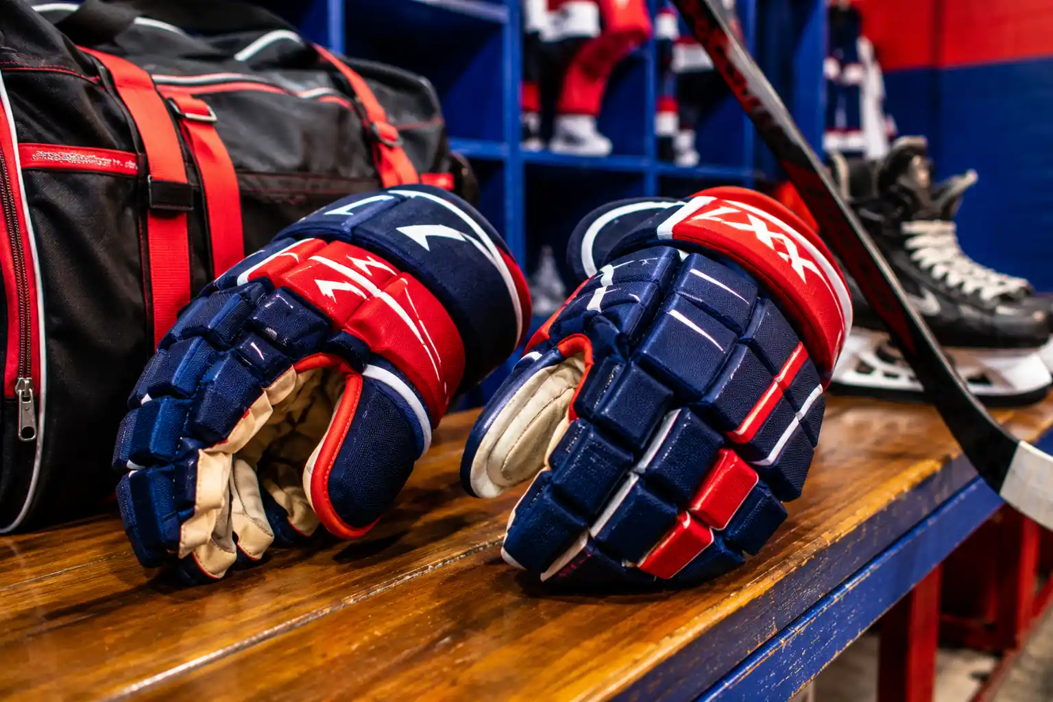 Gants de hockey sur glace posés sur un banc de vestiaire avec sac et crosse en arrière-plan