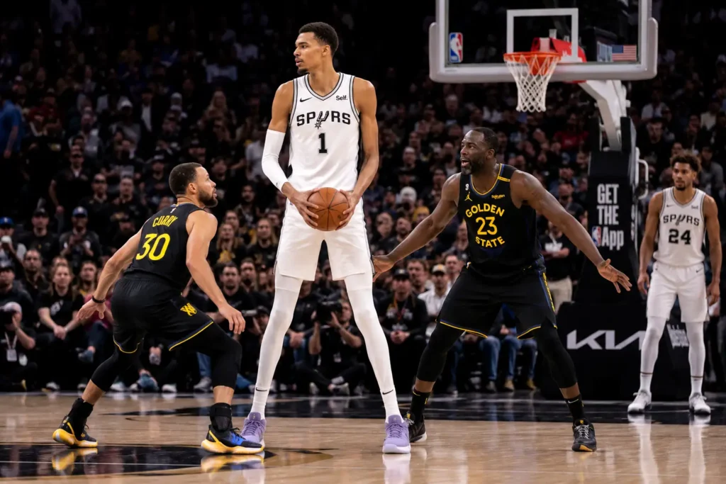 joueur de basket très grand tenant le ballon face à des défenseurs plus petits sur un parquet professionnel