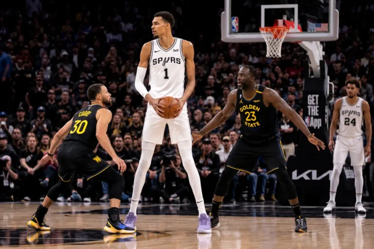 joueur de basket très grand tenant le ballon face à des défenseurs plus petits sur un parquet professionnel